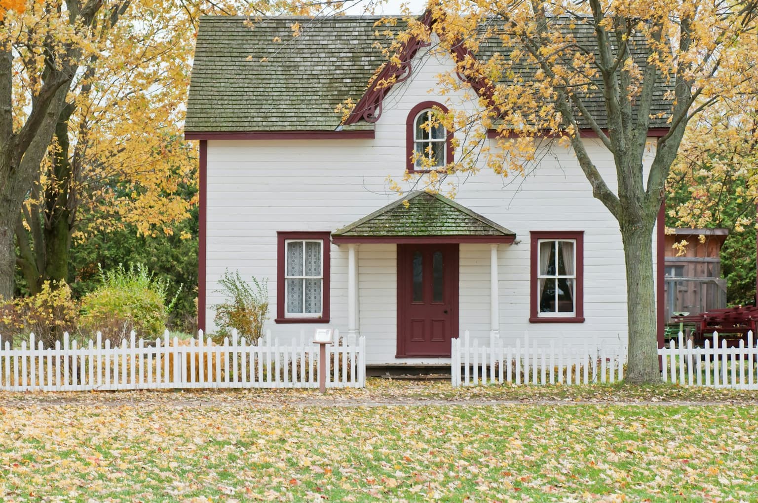 White cottage with a red door behind a picket fence in autumn