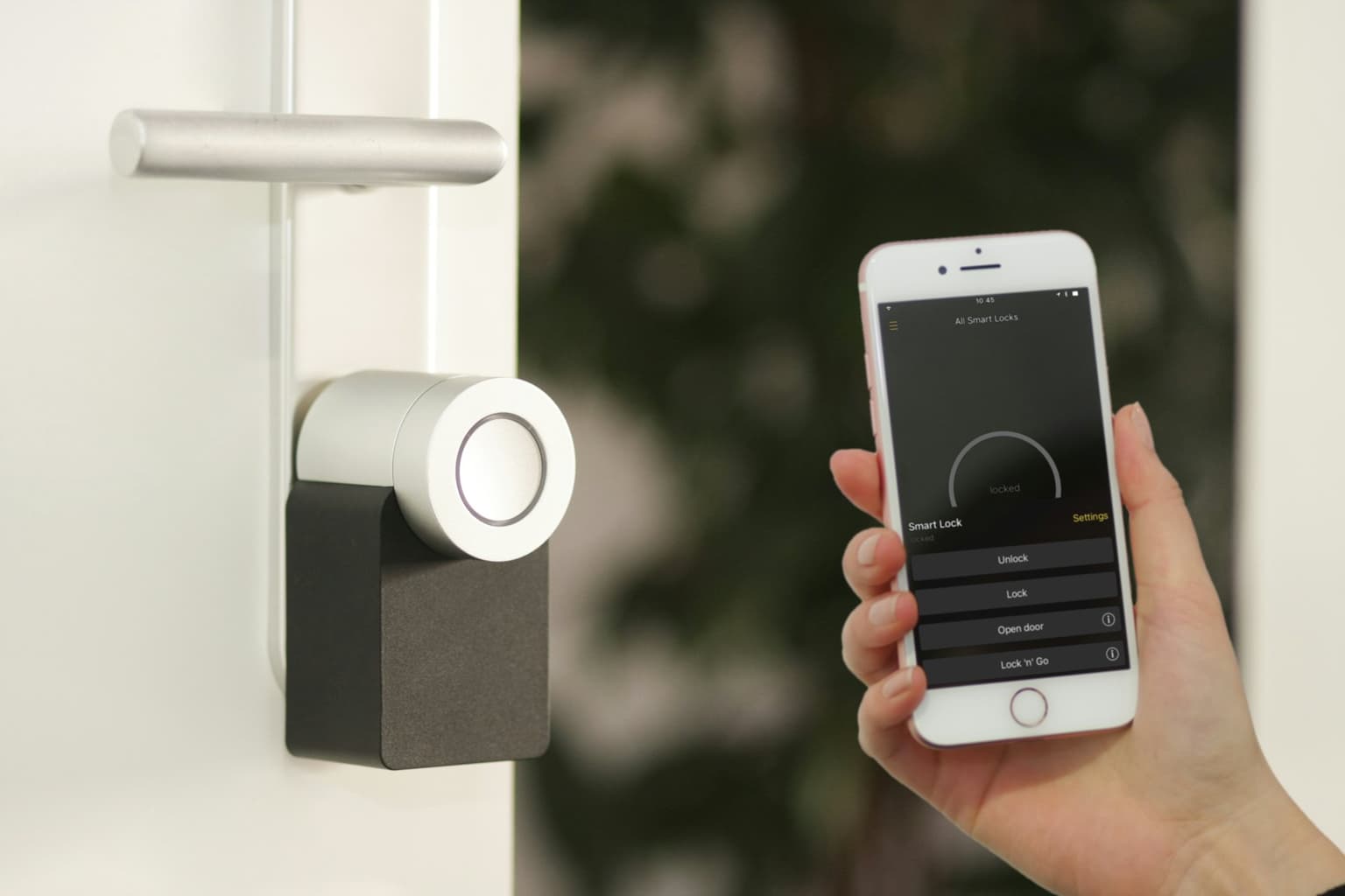 Hand holding a smartphone next to a smart home device on a door